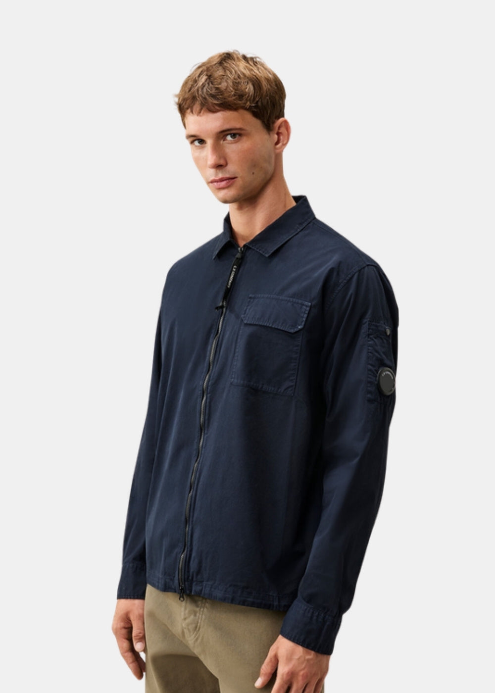 Porté de trois quarts d'une surchemise zippée marine C.P. Company en gabardine, montrant le col classique et la poche poitrine à rabat.