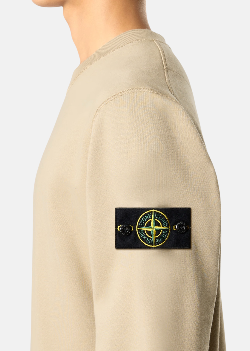 Zoom sur le badge Stone Island sur la manche d'un sweat beige à col rond porté de profil