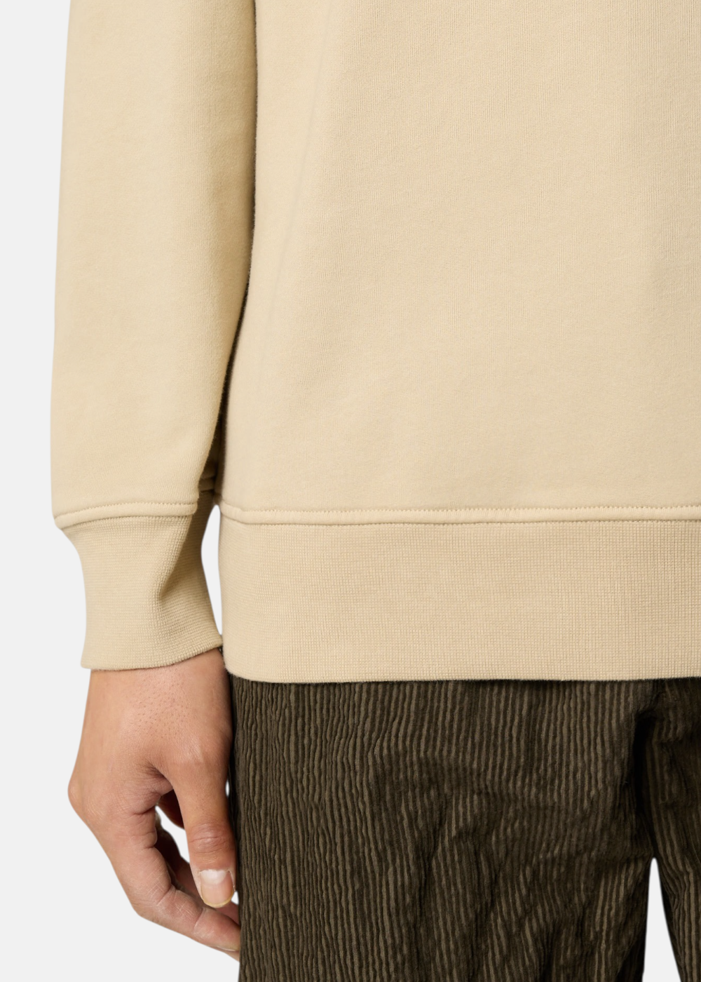 Gros plan sur le poignet et le bas côtelé d'un sweat beige Stone Island porté avec un pantalon en velours