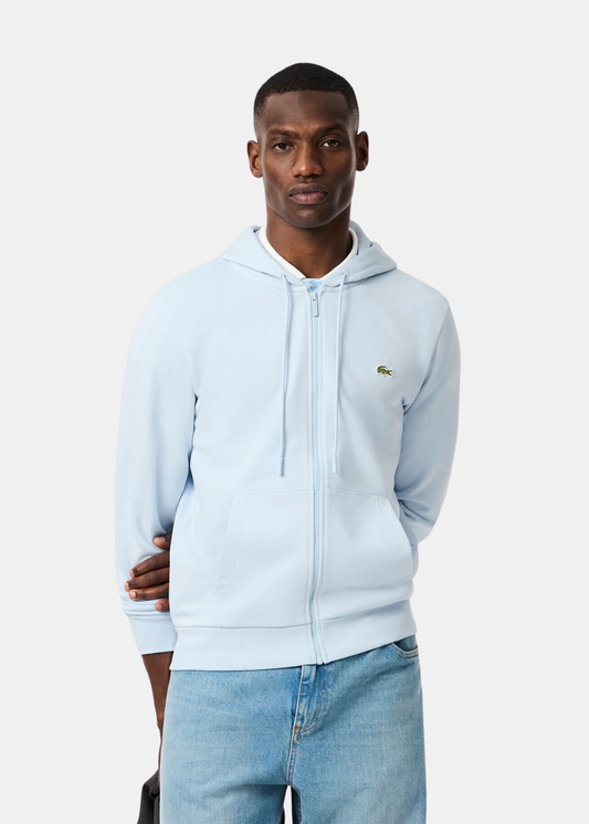 Vue de face d'un mannequin portant le sweatshirt zippé bleu ciel Lacoste, focus sur le buste et la capuche.