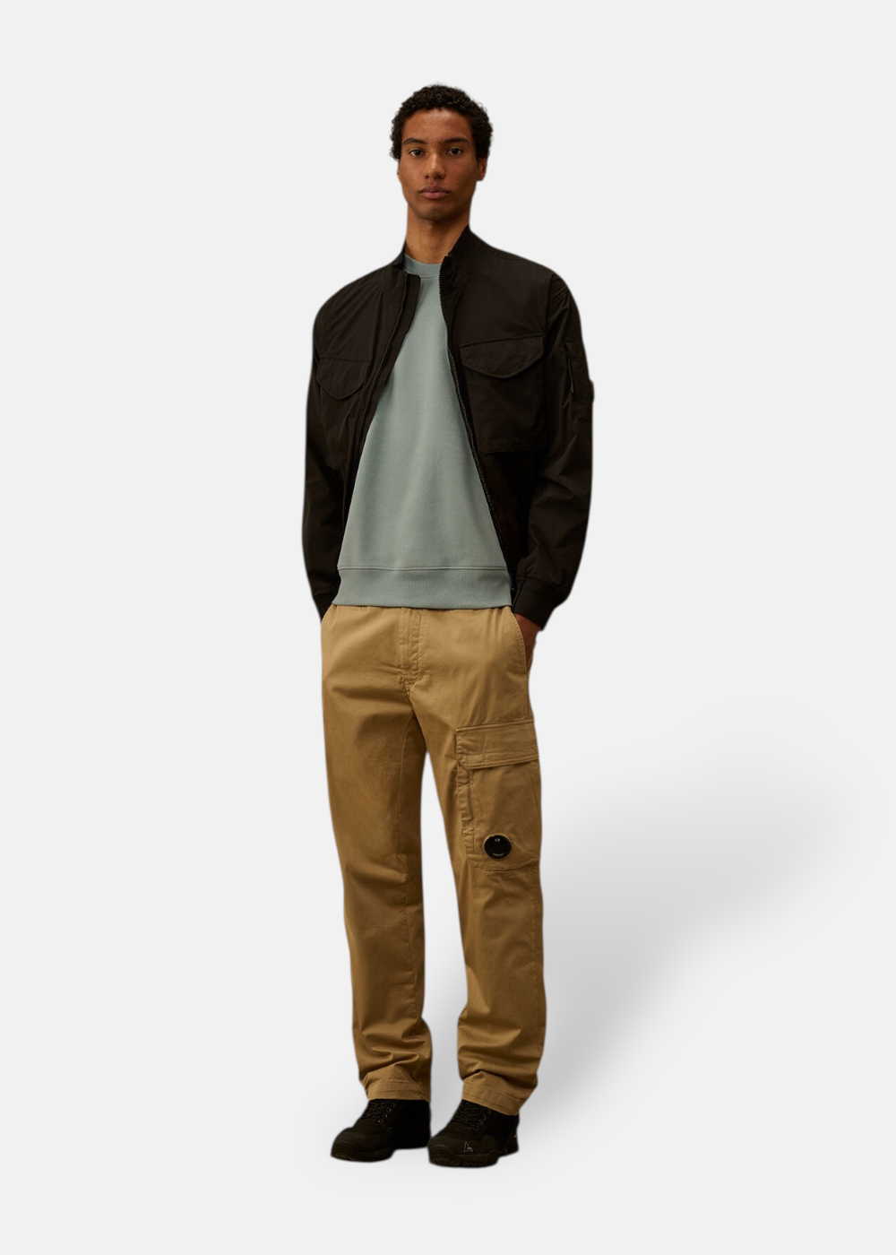 Silhouette complète avec blouson noir, sweat bleu gris, pantalon cargo beige et chaussures noires.