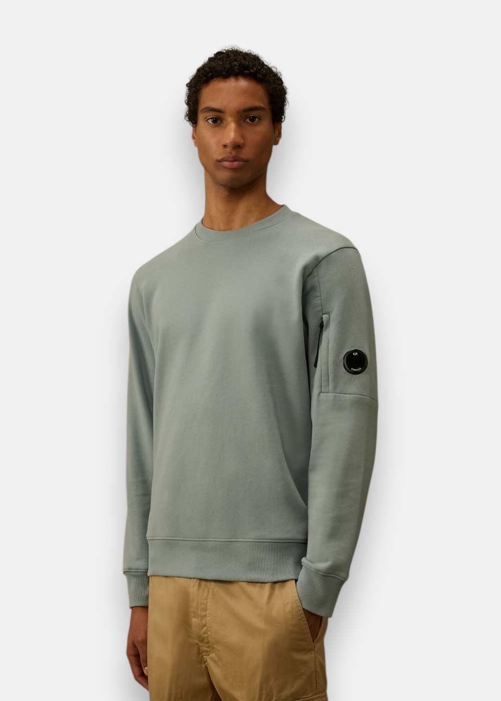 Sweat-shirt bleu gris C.P. Company porté de face par un mannequin avec un pantalon beige.