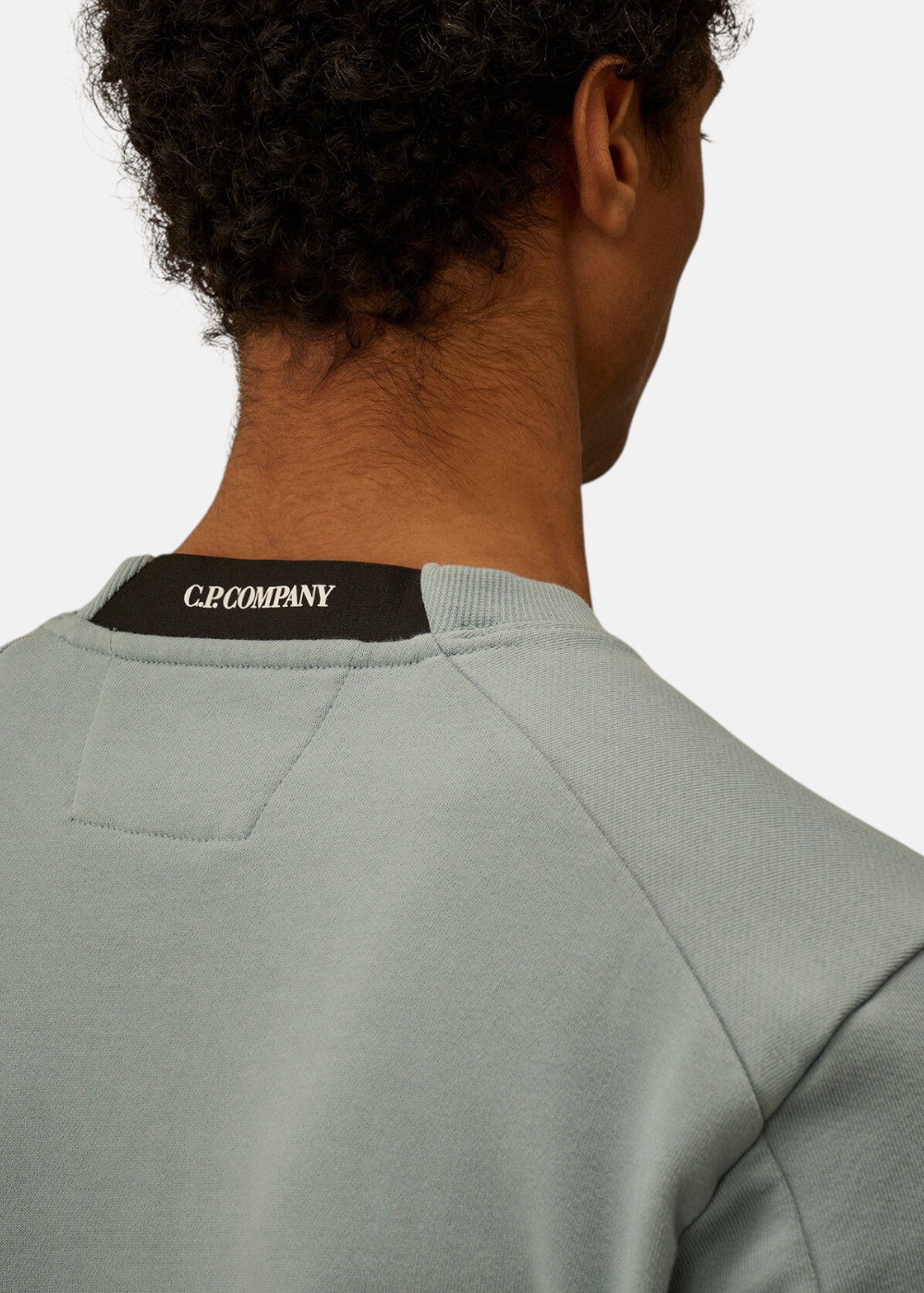 Gros plan sur le dos du col du sweat-shirt bleu gris avec l'inscription C.P. Company brodée en blanc.