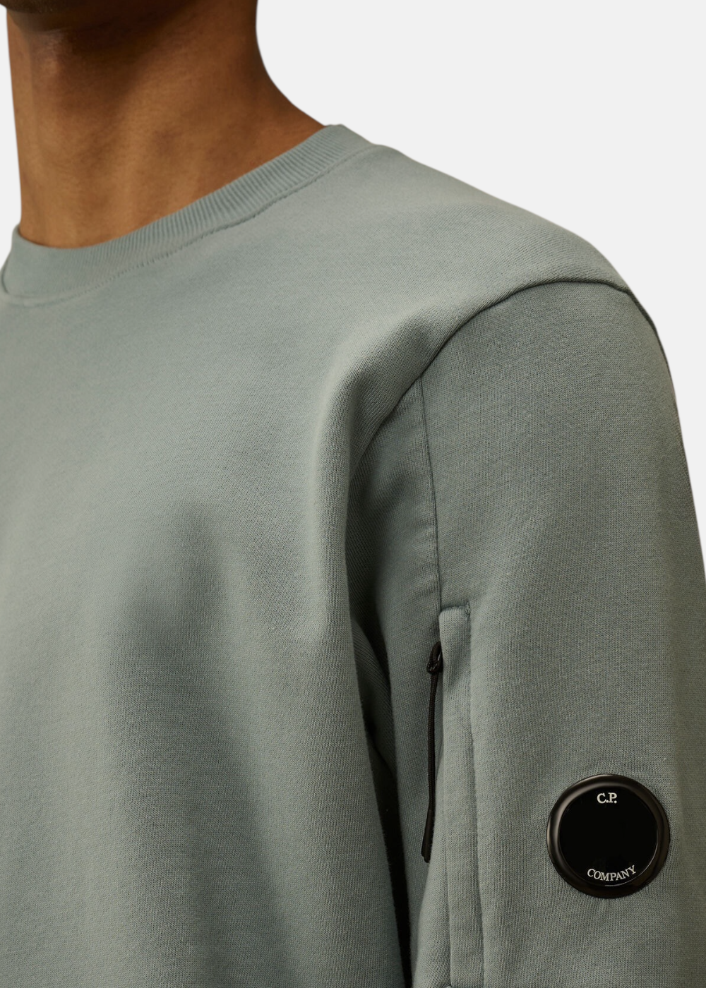 Zoom sur le bras du mannequin portant le sweat bleu gris avec la lentille Lens noire sur la poche.