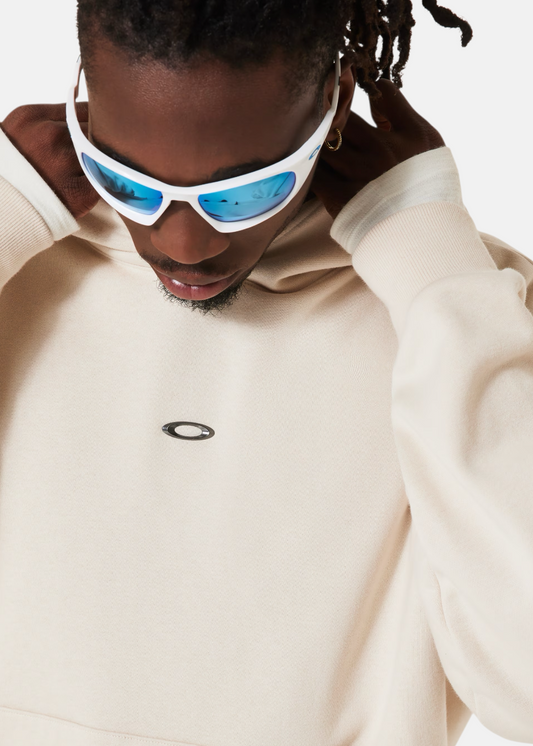 Gros plan sur le logo Oakley iconique avec une finition métallisée sur le molleton beige sable.