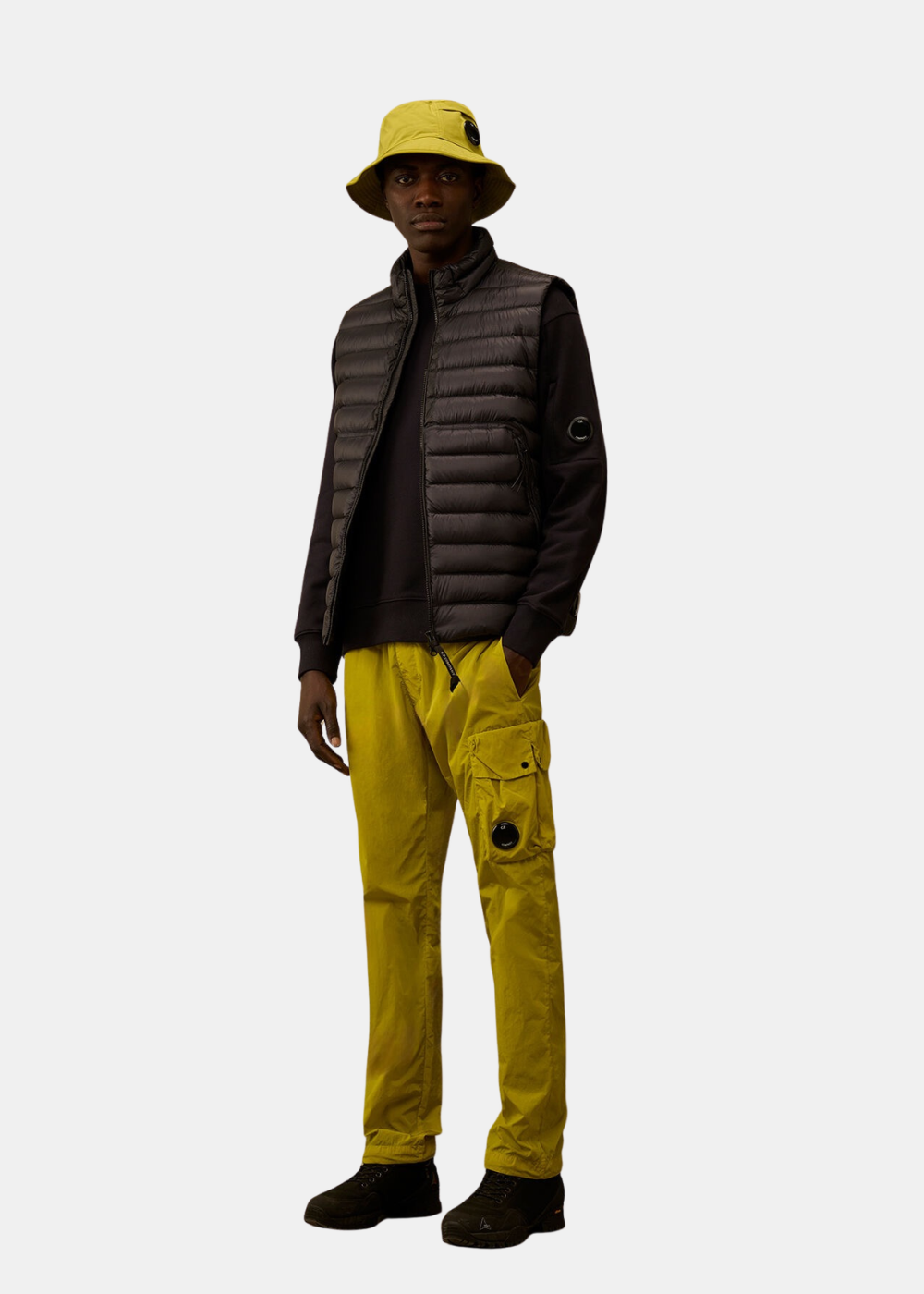 Look complet avec sweat marine C.P. Company, sans-manche noir, pantalon cargo et bob jaune moutarde.