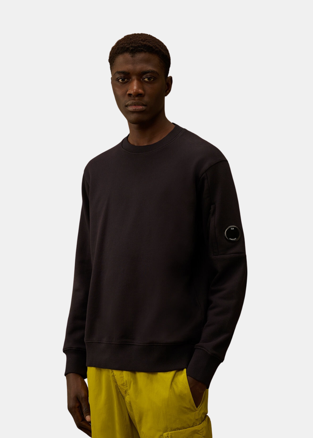 Homme portant un sweat marine C.P. Company col rond avec détail lentille sur la manche gauche.