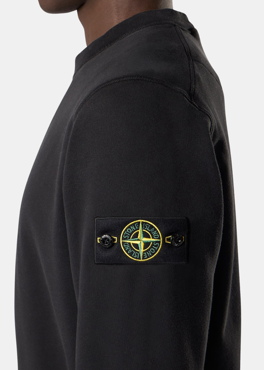 Gros plan de profil sur la manche d'un sweat noir en molleton Stone Island avec son badge boussole boutonné.