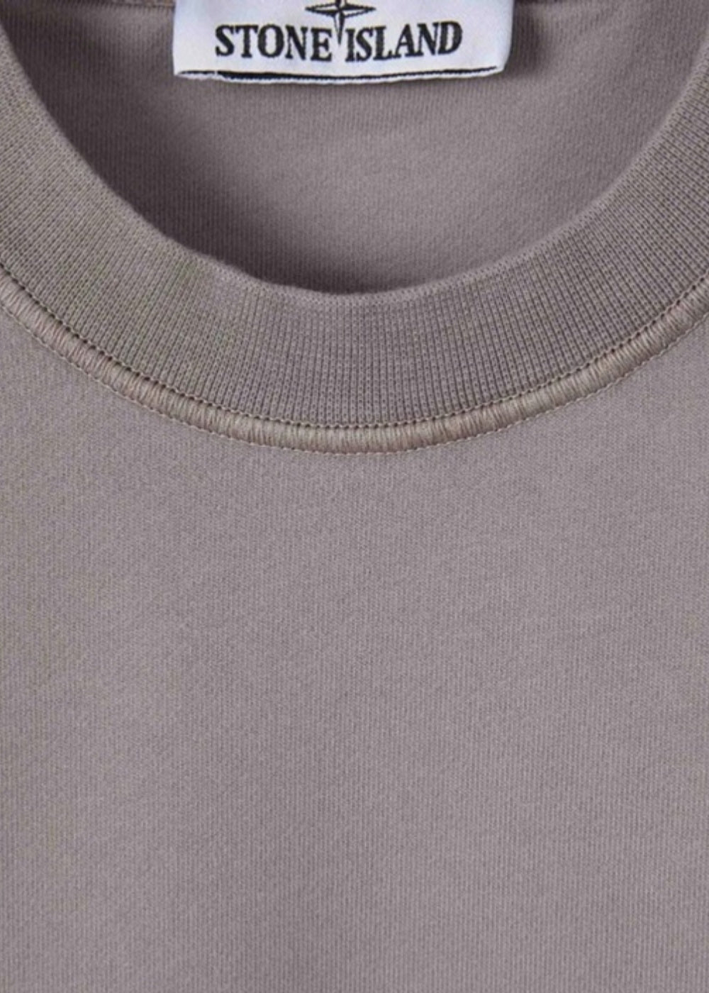 Gros plan sur le col rond côtelé d'un sweat-shirt gris Stone Island et son étiquette brodée à la marque, sur jersey uni.