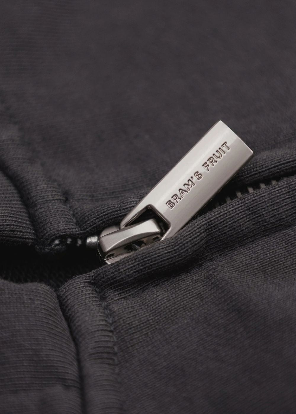 Gros plan sur le tirette de la fermeture éclair gravée du nom de la marque Bram's Fruit