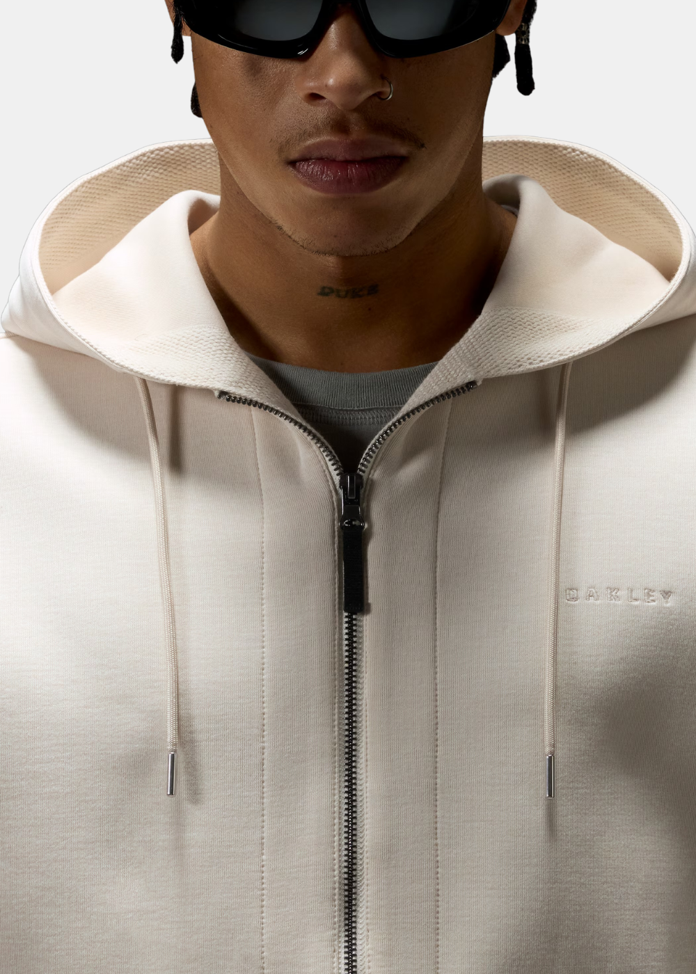 Zoom sur le logo Oakley brodé ton sur ton sur la poitrine et la fermeture éclair du sweat beige.