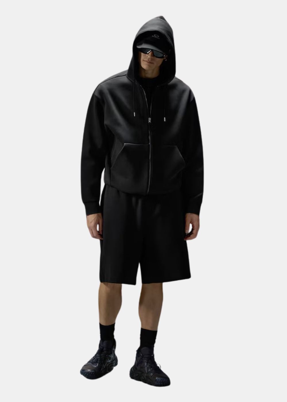 Look complet avec sweat à capuche noir Oakley, short assorti, casquette et baskets techniques sombres.