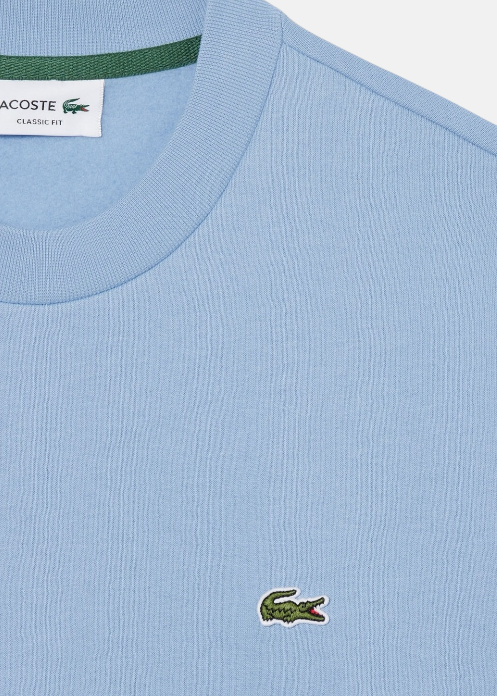 Gros plan sur le logo crocodile vert emblématique brodé sur la poitrine du sweatshirt bleu Lacoste.