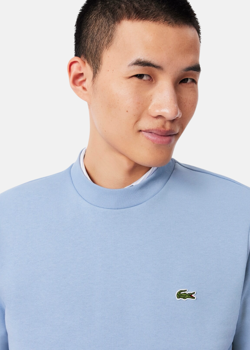 Gros plan sur le buste d'un homme portant le sweatshirt bleu Lacoste mettant en avant le col rond et le logo.