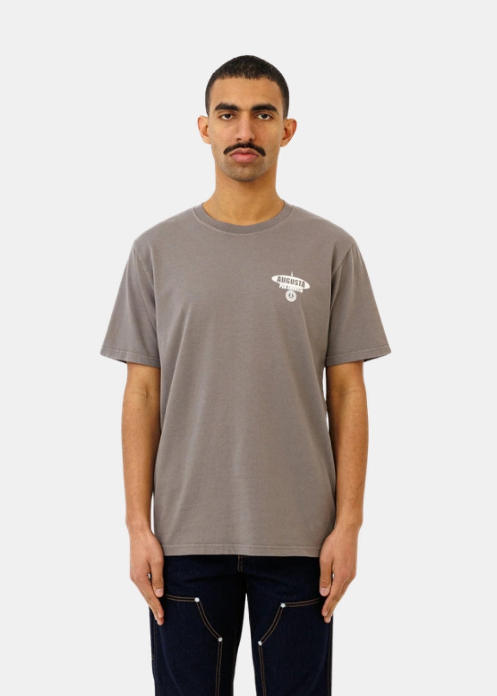 Porté de face d'un t-shirt gris Ateliers de Nîmes AD AUGUSTA à petit motif poitrine, associé à un pantalon bleu foncé.