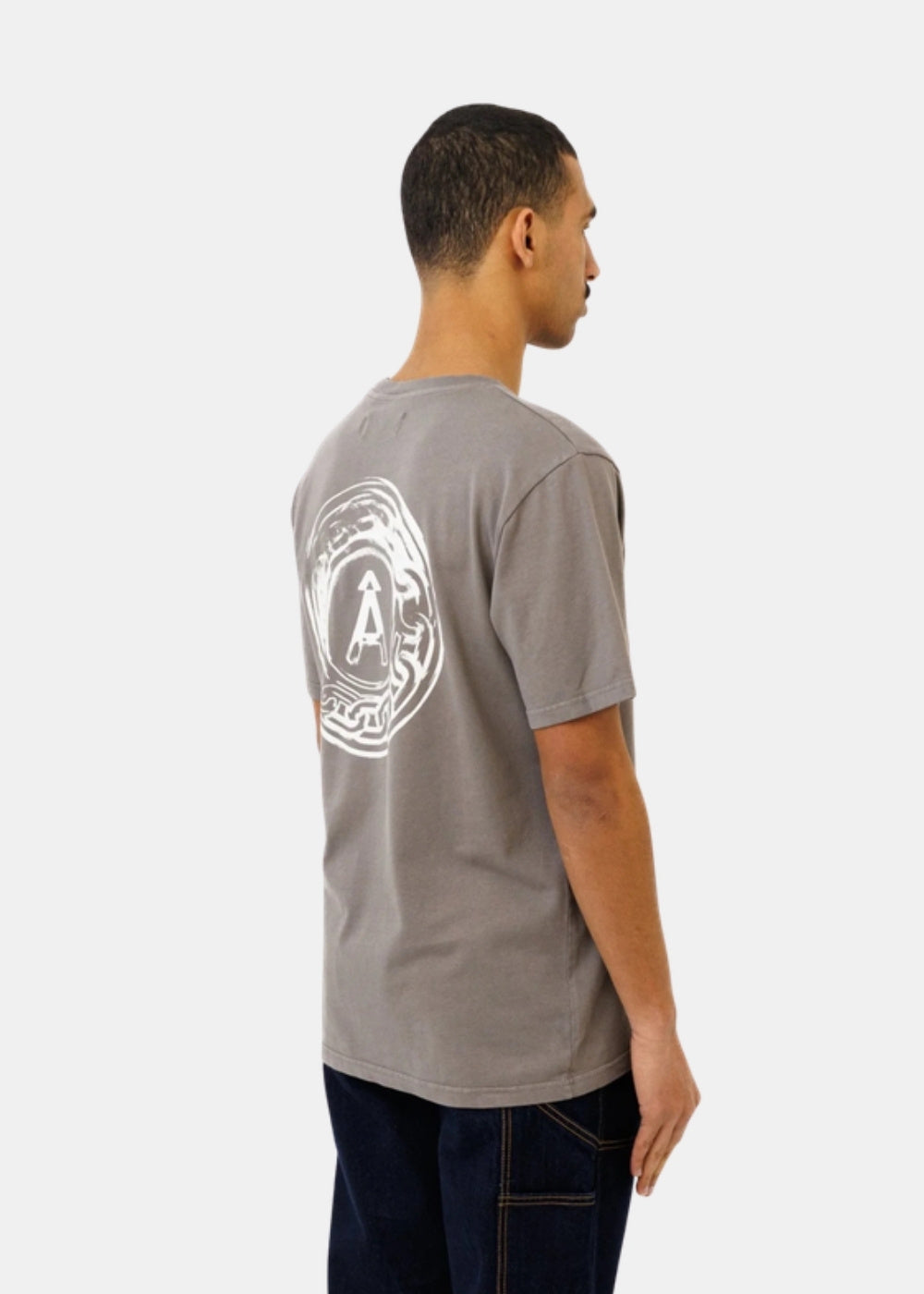 Porté de profil d'un t-shirt gris Ateliers de Nîmes AD AUGUSTA montrant la coupe ample et l'emblème sérigraphié au dos.