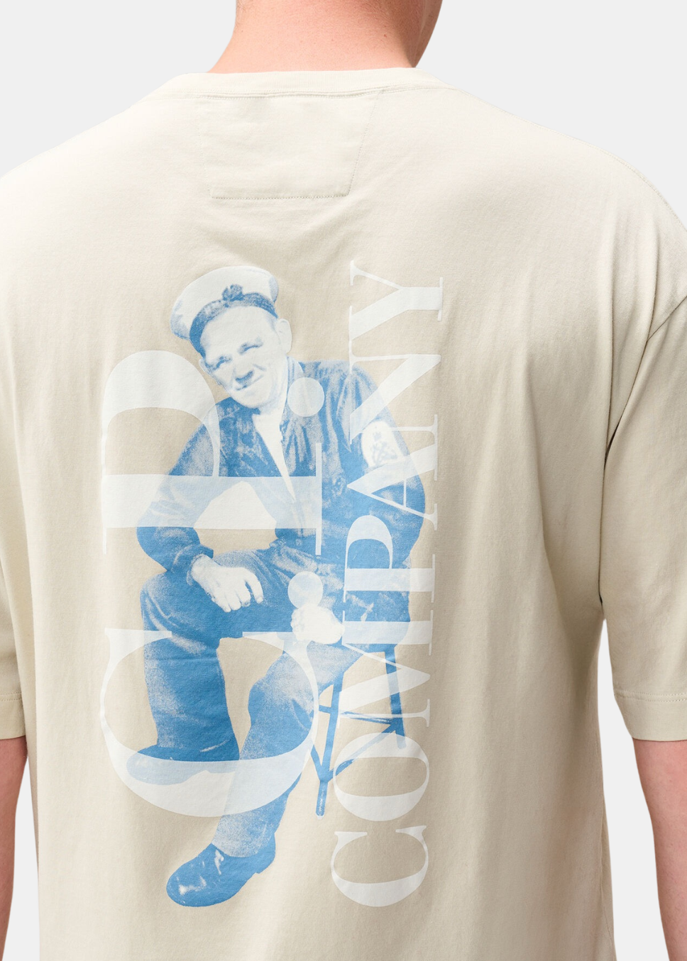 Gros plan sur le visuel dos du t-shirt beige C.P. Company représentant une illustration de marin marinier en bleu avec typographie C.P. Company en transparence