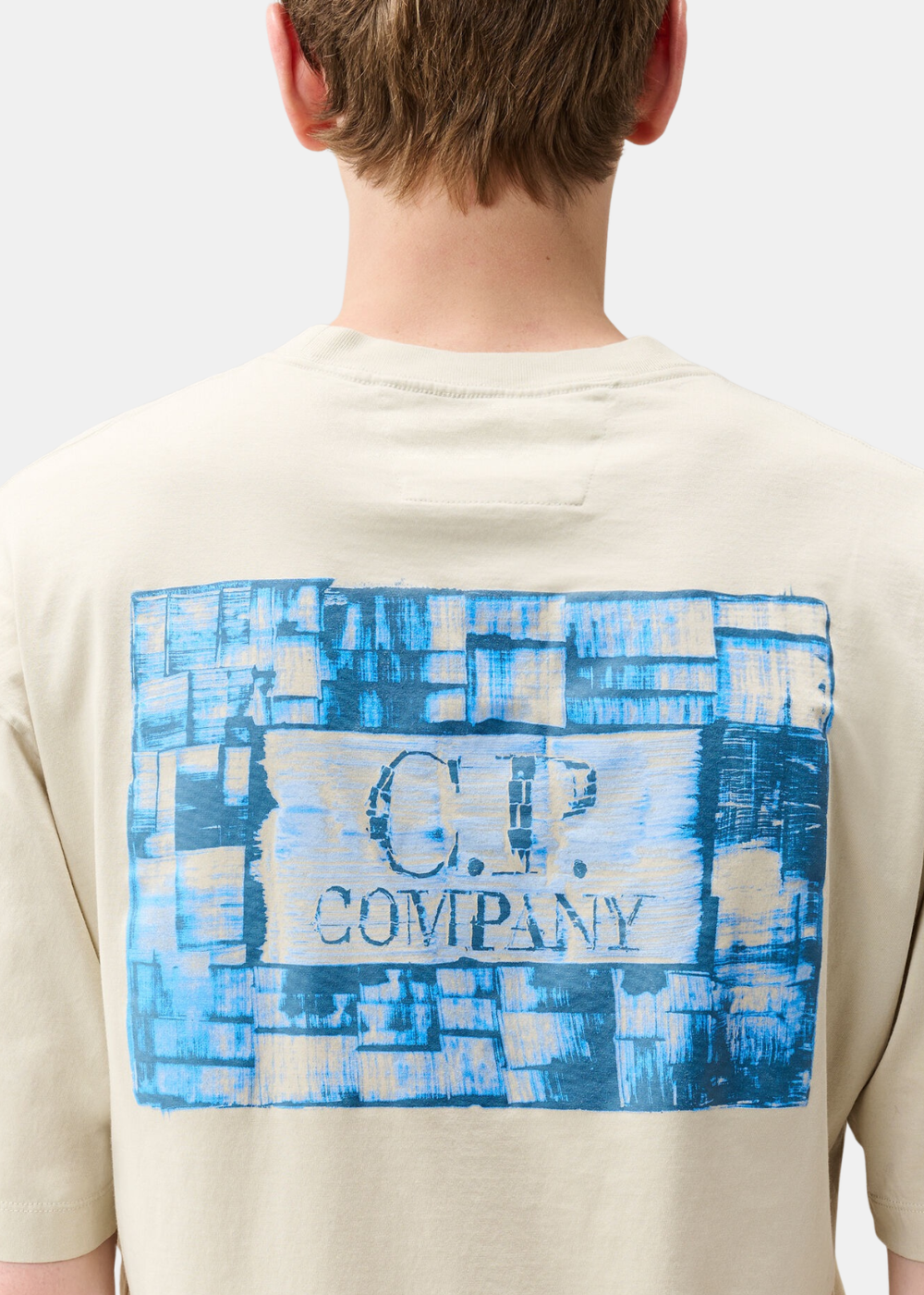 Gros plan de dos sur le grand imprimé graphique brossé bleu et blanc C.P. Company d'un t-shirt beige.