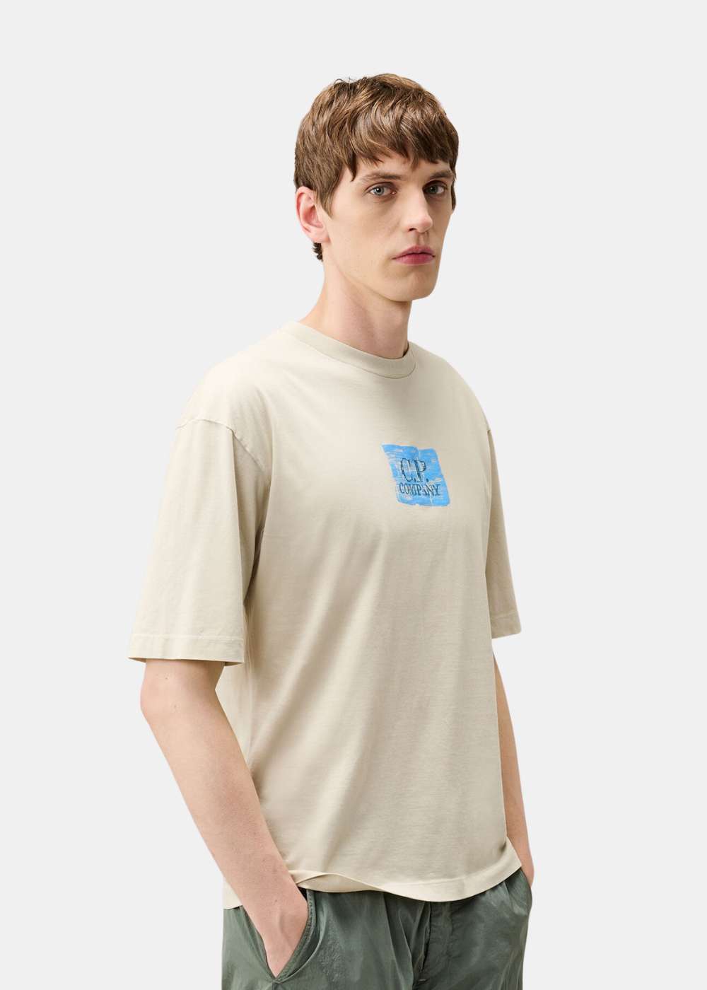 T-shirt en coton beige C.P. Company porté de trois-quarts face par un mannequin avec un short kaki.