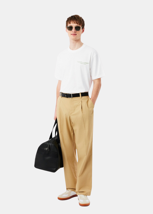 Mannequin de face portant le t-shirt blanc Lacoste avec un pantalon à pinces beigeet des baskets blanches.