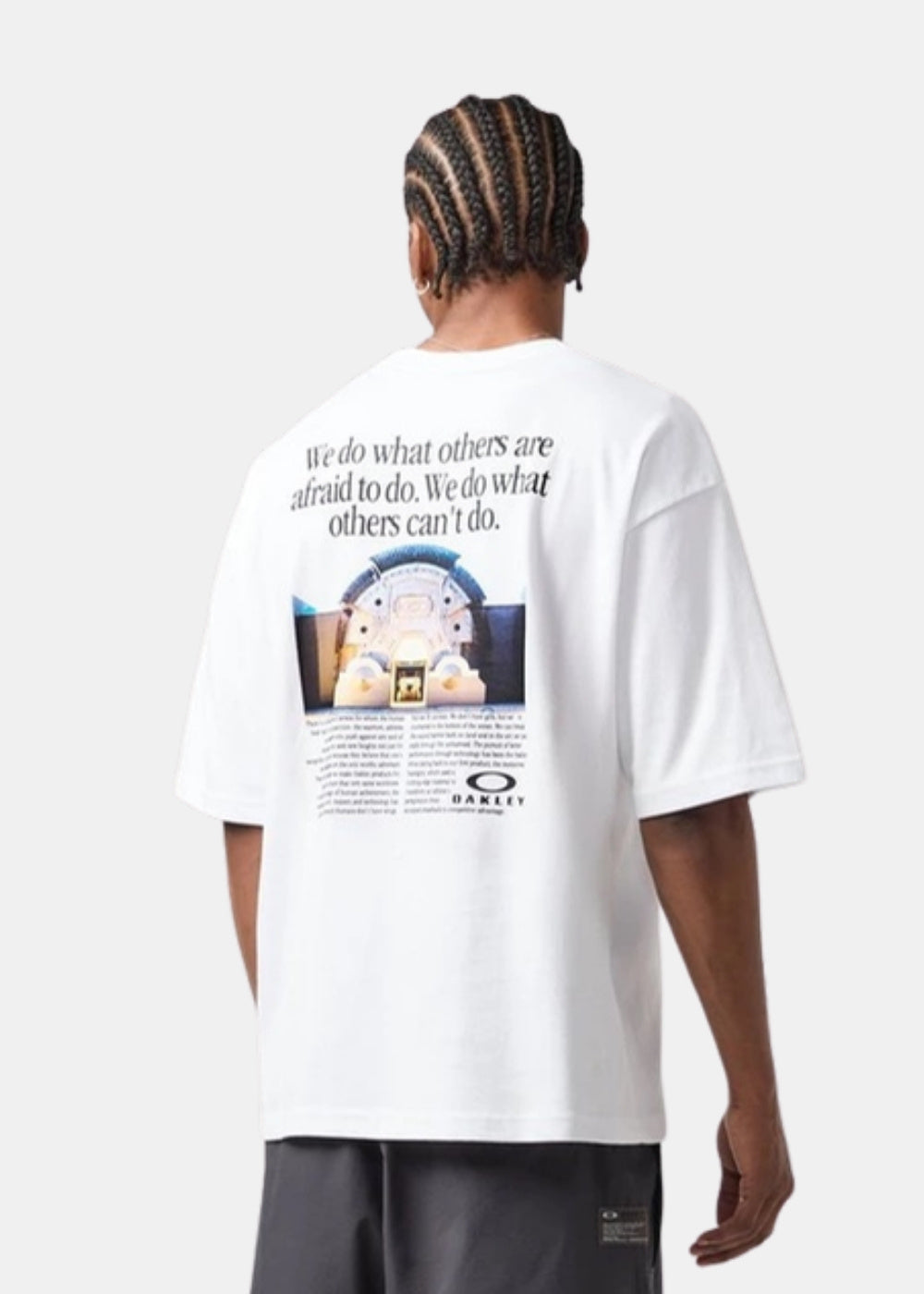 Porté de dos d'un t-shirt blanc Oakley oversize montrant le visuel imprimé, le texte et le logo en bas du graphisme sur fond neutre.