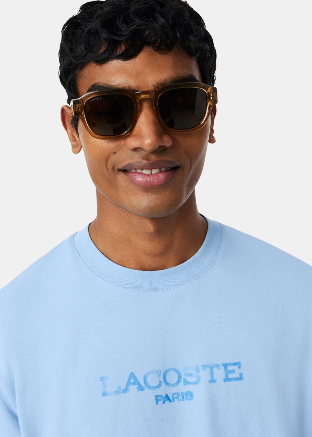 Gros plan sur le haut du t-shirt Lacoste bleu ciel, montrant les détails du col rond et du marquage Lacoste Paris texturé.