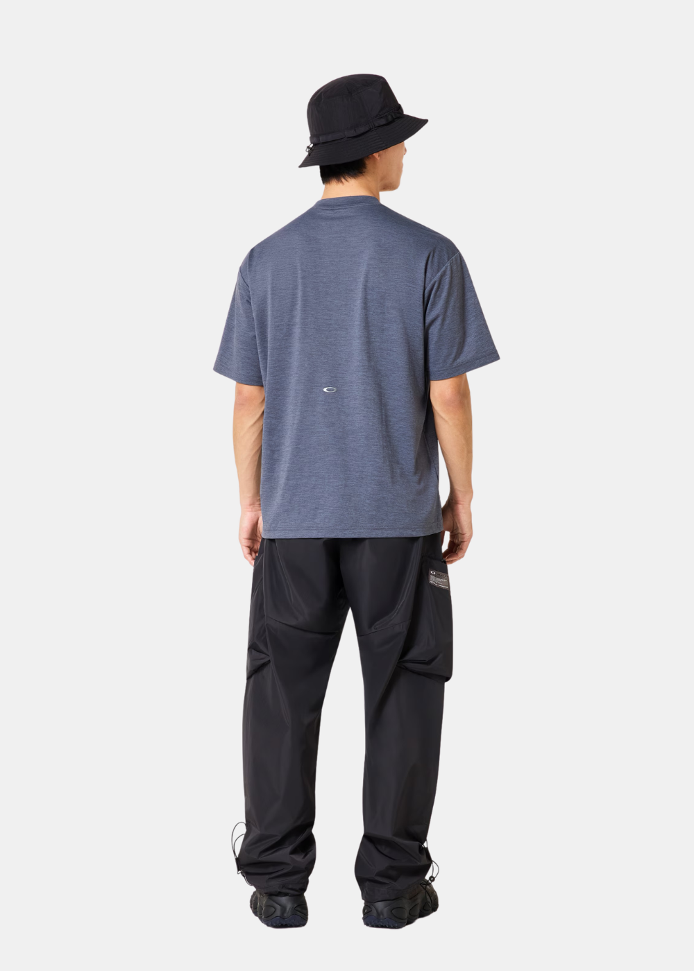 Homme de dos portant le t-shirt bleu Oakley avec un petit logo au centre et un pantalon noir.