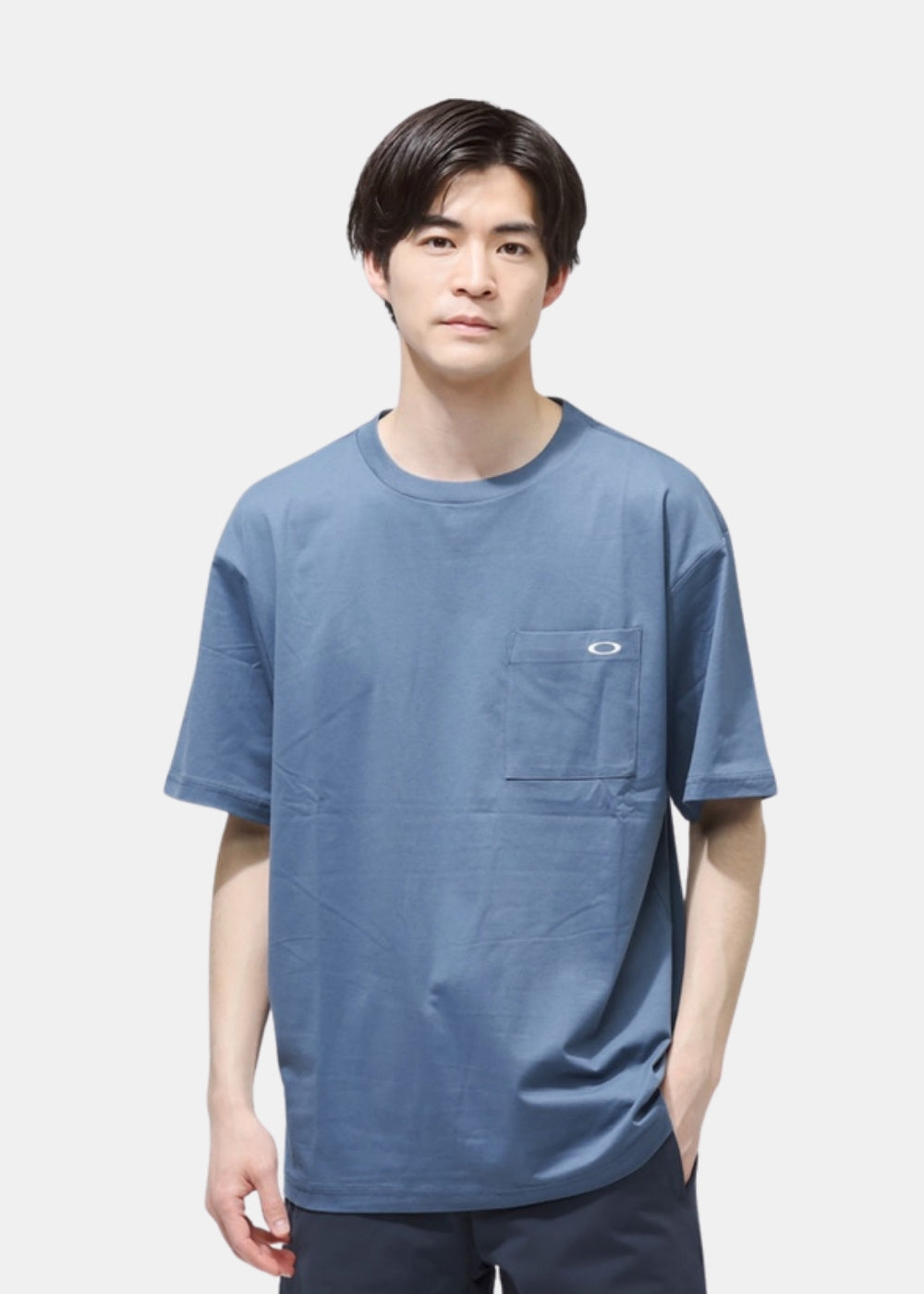 Porté de face d'un t-shirt bleu Oakley à col rond et poche poitrine, coupe droite et manches courtes.