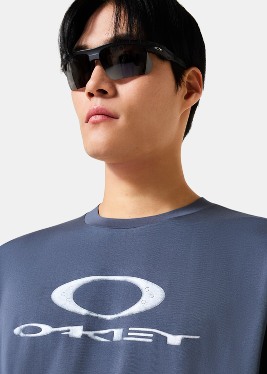 Plan rapproché d'un homme portant le t-shirt bleu Oakley avec grand logo blanc sur le torse.