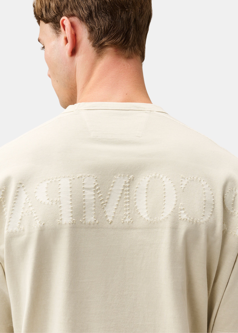 Gros plan sur le lettrage C.P. Company cousu en empiècements textile au dos du t-shirt beige