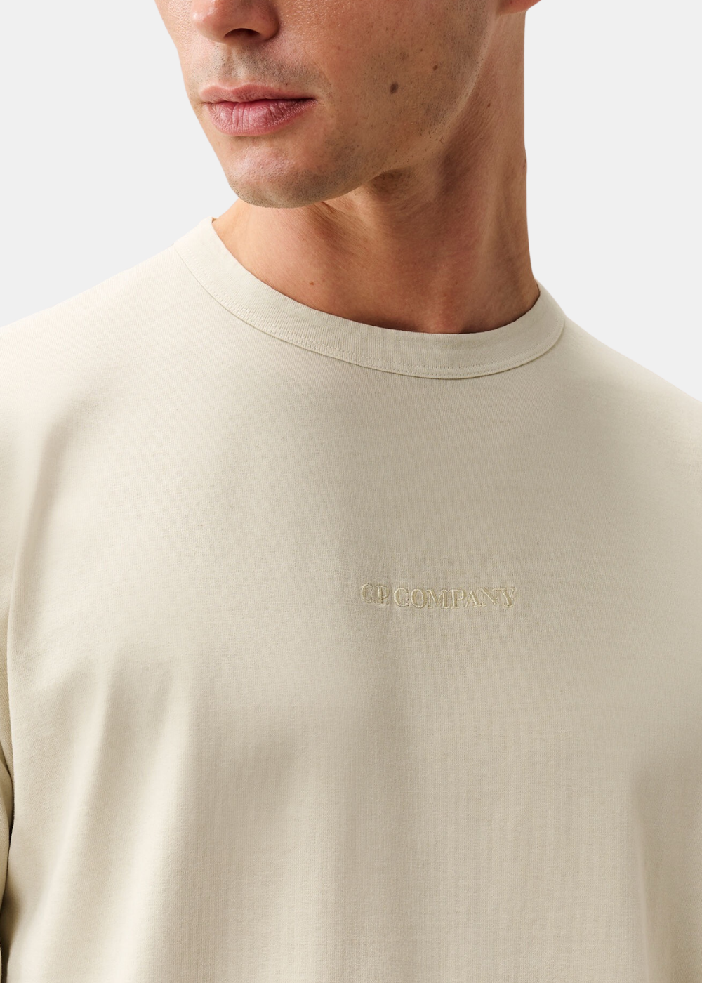 Gros plan sur le col rond et la broderie C.P. Company ton sur ton au centre du t-shirt beige