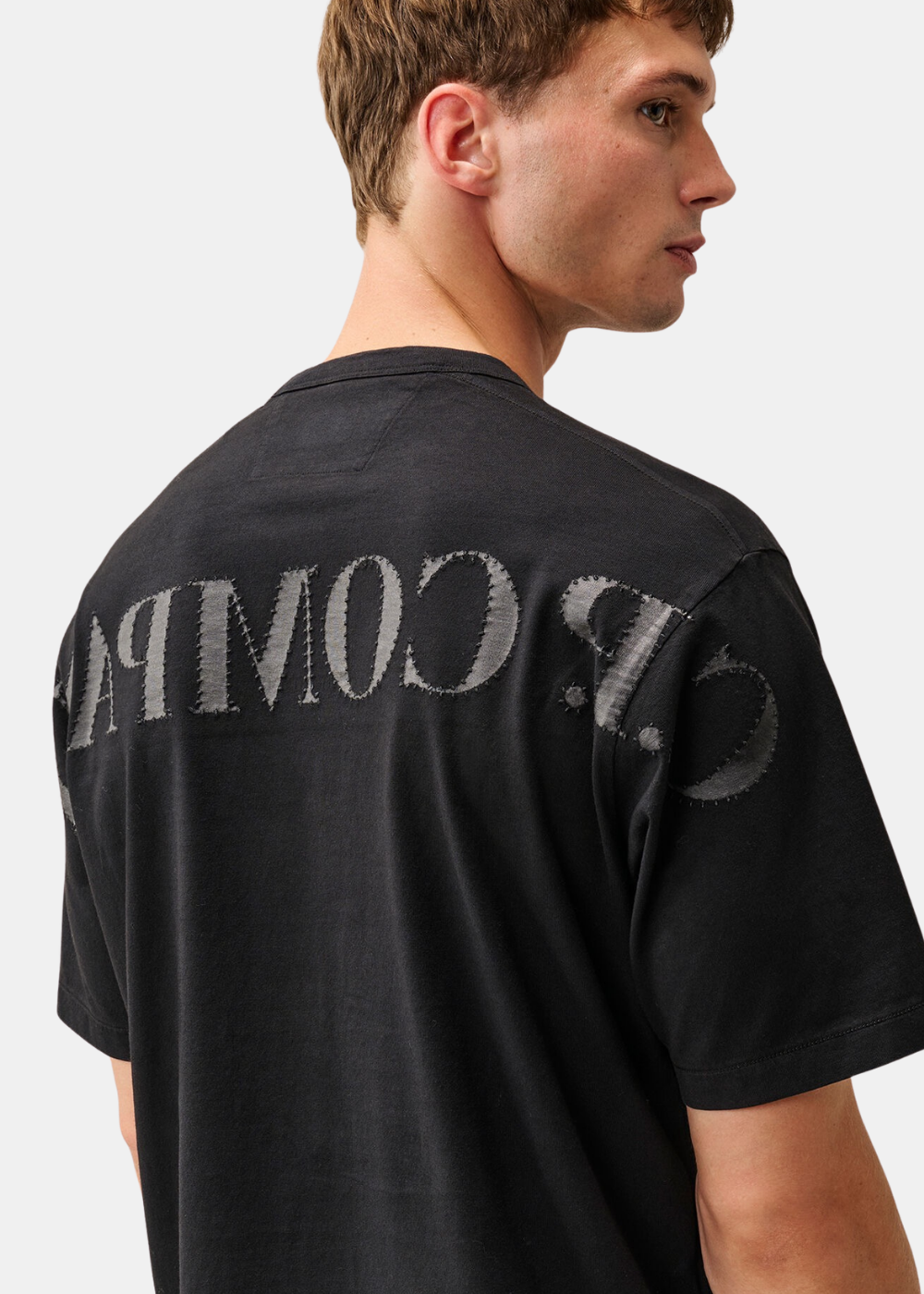 Gros plan sur le logo C.P. Company en empiècements textile cousus au dos du t-shirt noir