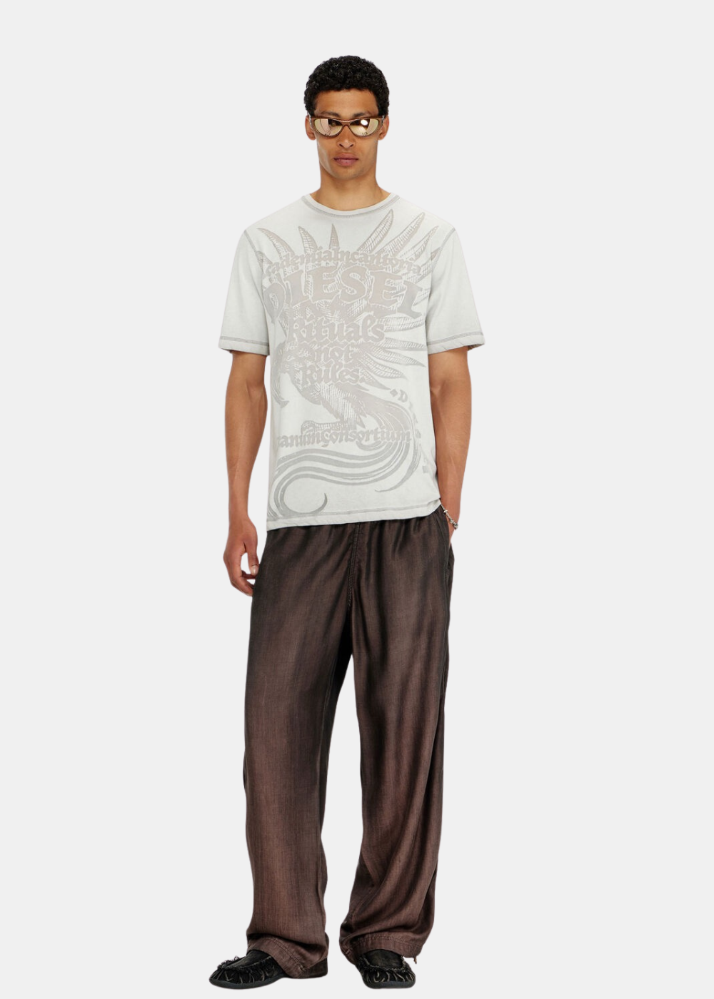 Look complet homme avec t-shirt gris clair imprimé, pantalon large marron satiné, lunettes dorées et chaussures noires.