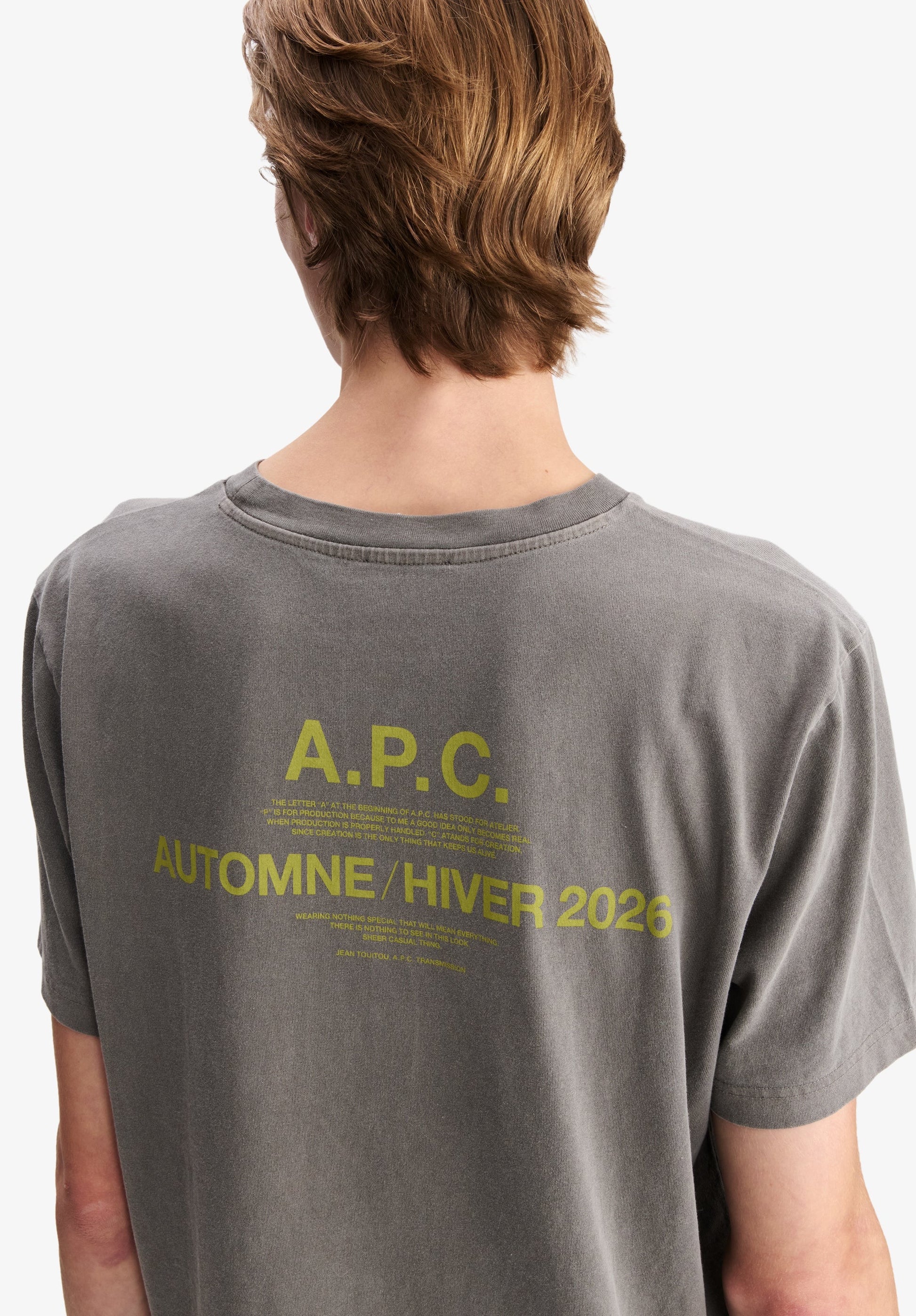Gros plan sur la sérigraphie jaune au dos du t-shirt gris délavé A.P.C. affichant « A.P.C. AUTOMNE / HIVER 2026 » et un texte explicatif