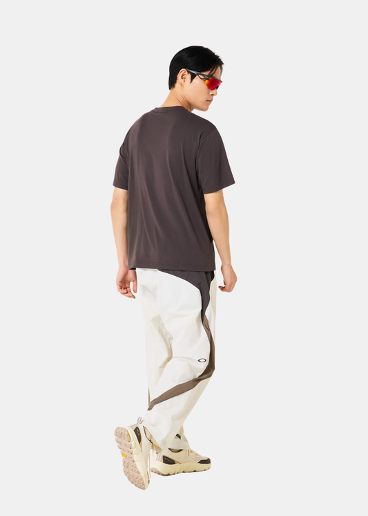 Vue de dos d'un homme portant le t-shirt gris Oakley avec un pantalon technique blanc et beige.