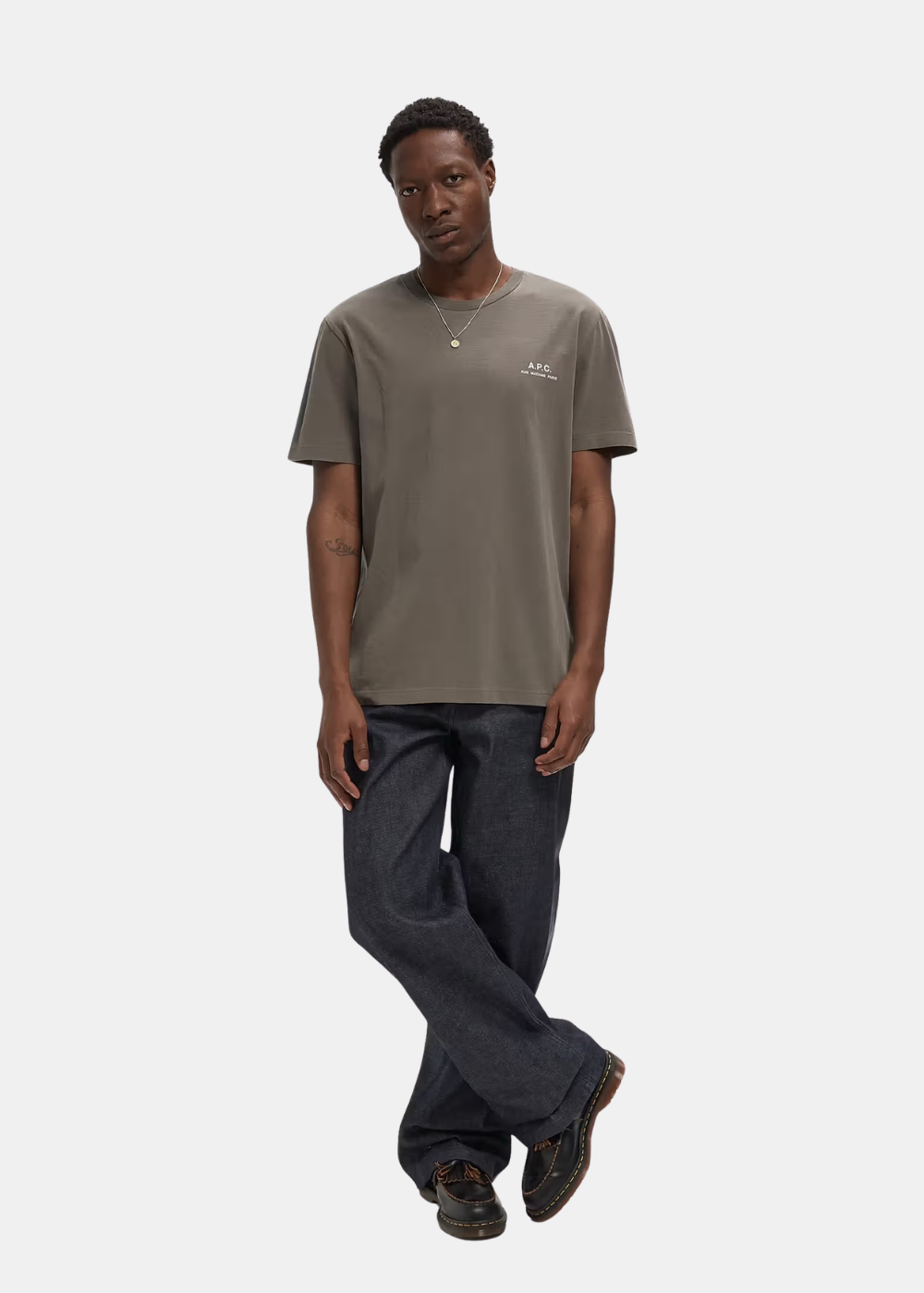 Mannequin homme de face en pied portant le t-shirt gris taupe A.P.C. avec un jean brut large, un collier chaîne et des mocassins en cuir noir
