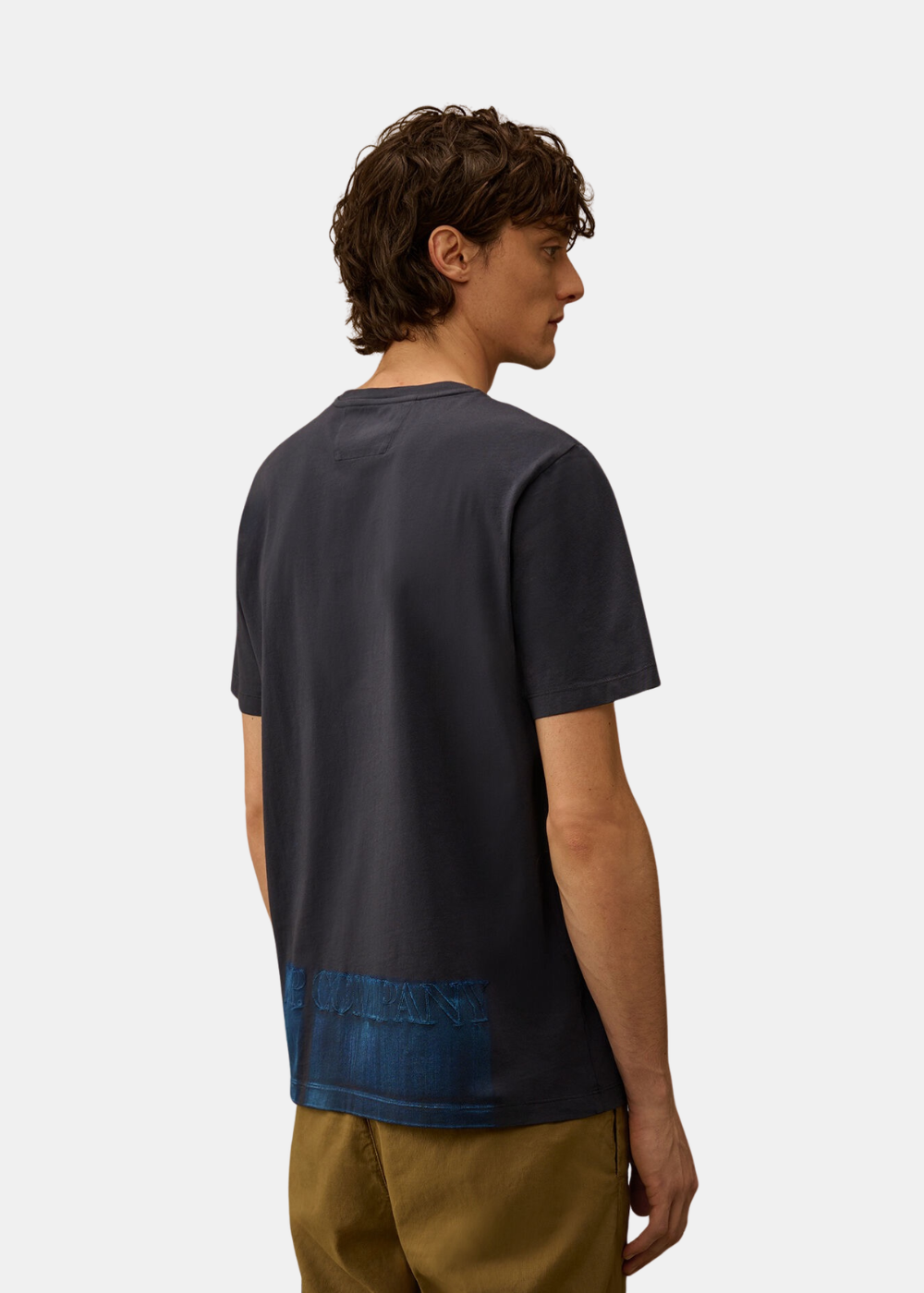 Vue de trois-quarts dos du mannequin portant le t-shirt bleu avec le grand logo C.P. Company imprimé à la base