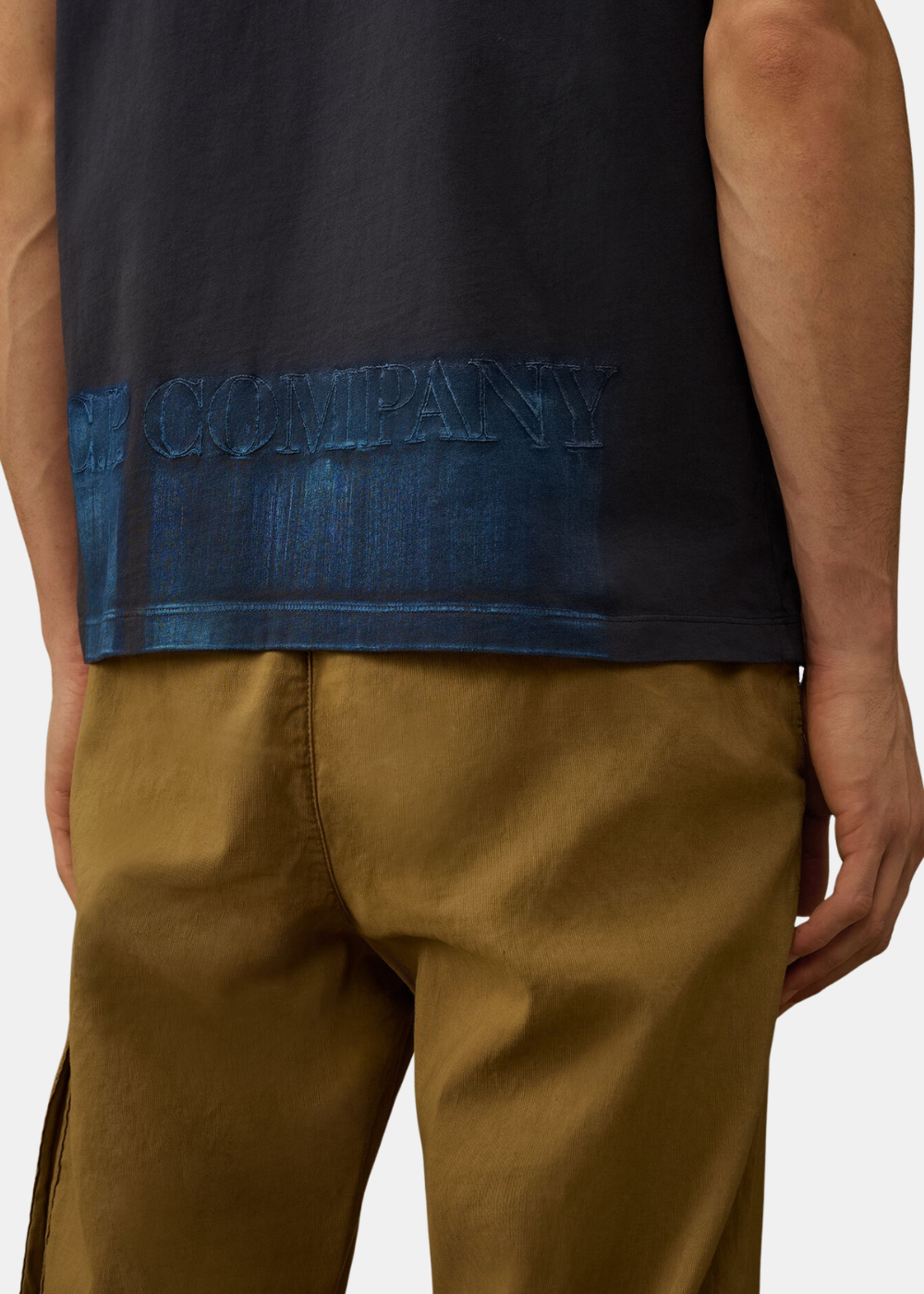 Zoom sur le bas du t-shirt bleu teint en pièce montrant l'effet délavé et l'inscription C.P. Company imprimée