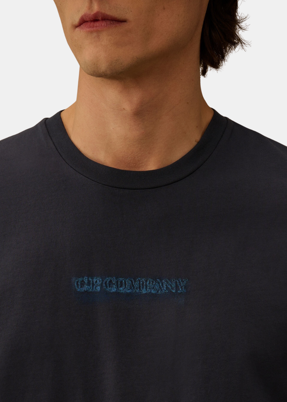 Gros plan sur le col rond et le petit logo texturé C.P. Company brodé en bleu sur la poitrine du t-shirt