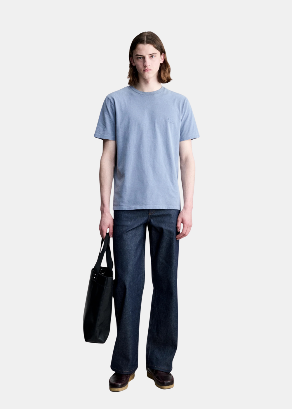 Mannequin homme en pied portant le t-shirt A.P.C. bleu délavé avec un jean brut et un cabas noir