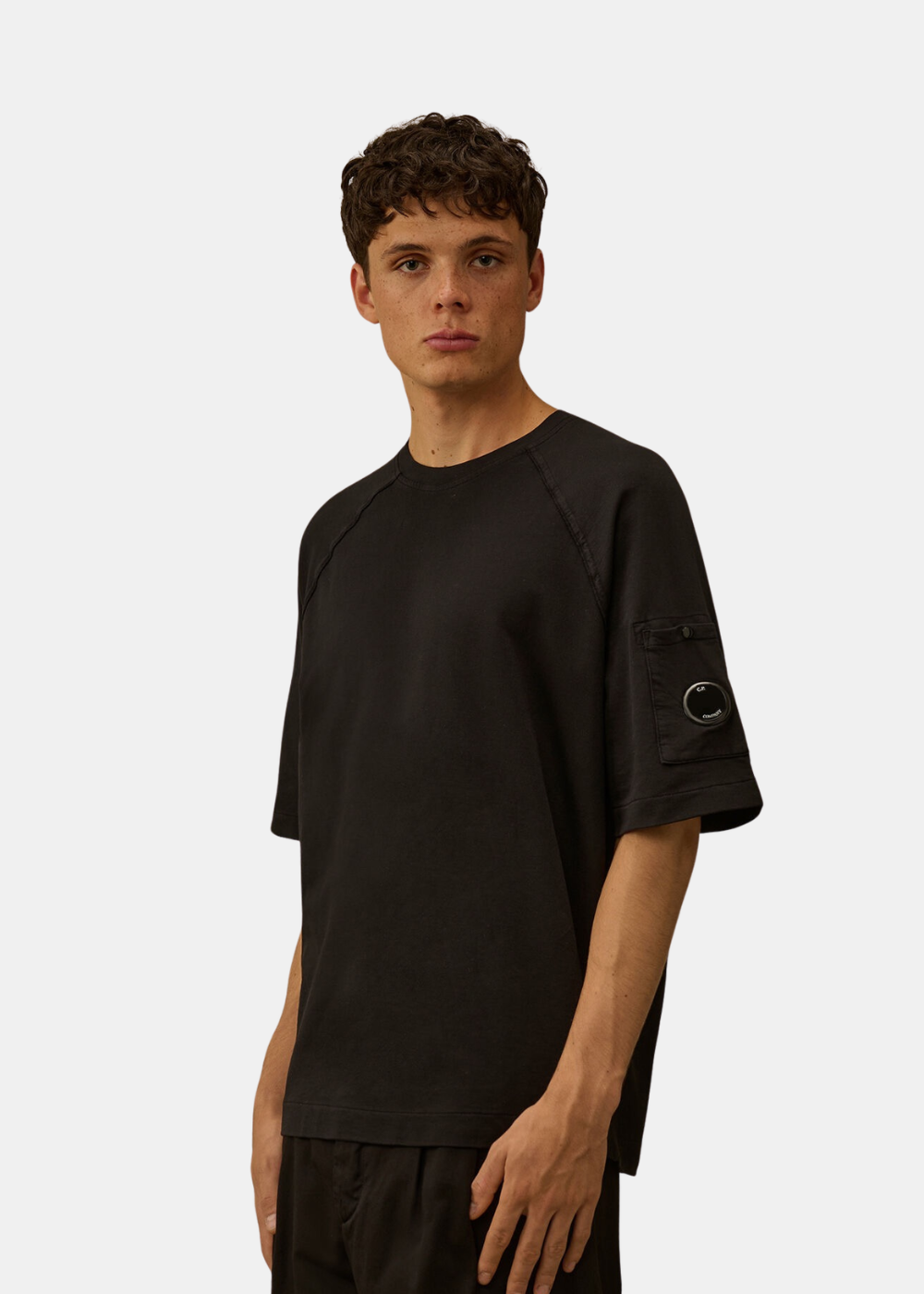 Mannequin homme de trois-quarts face portant le t-shirt en molleton C.P. Company noir, mettant en valeur la coupe décontractée et le détail de la lentille noire sur le bras