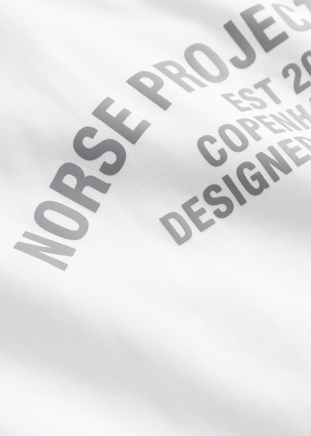 Gros plan sur l'imprimé gris Norse Projects en forme d'arche sur le t-shirt Homme blanc.