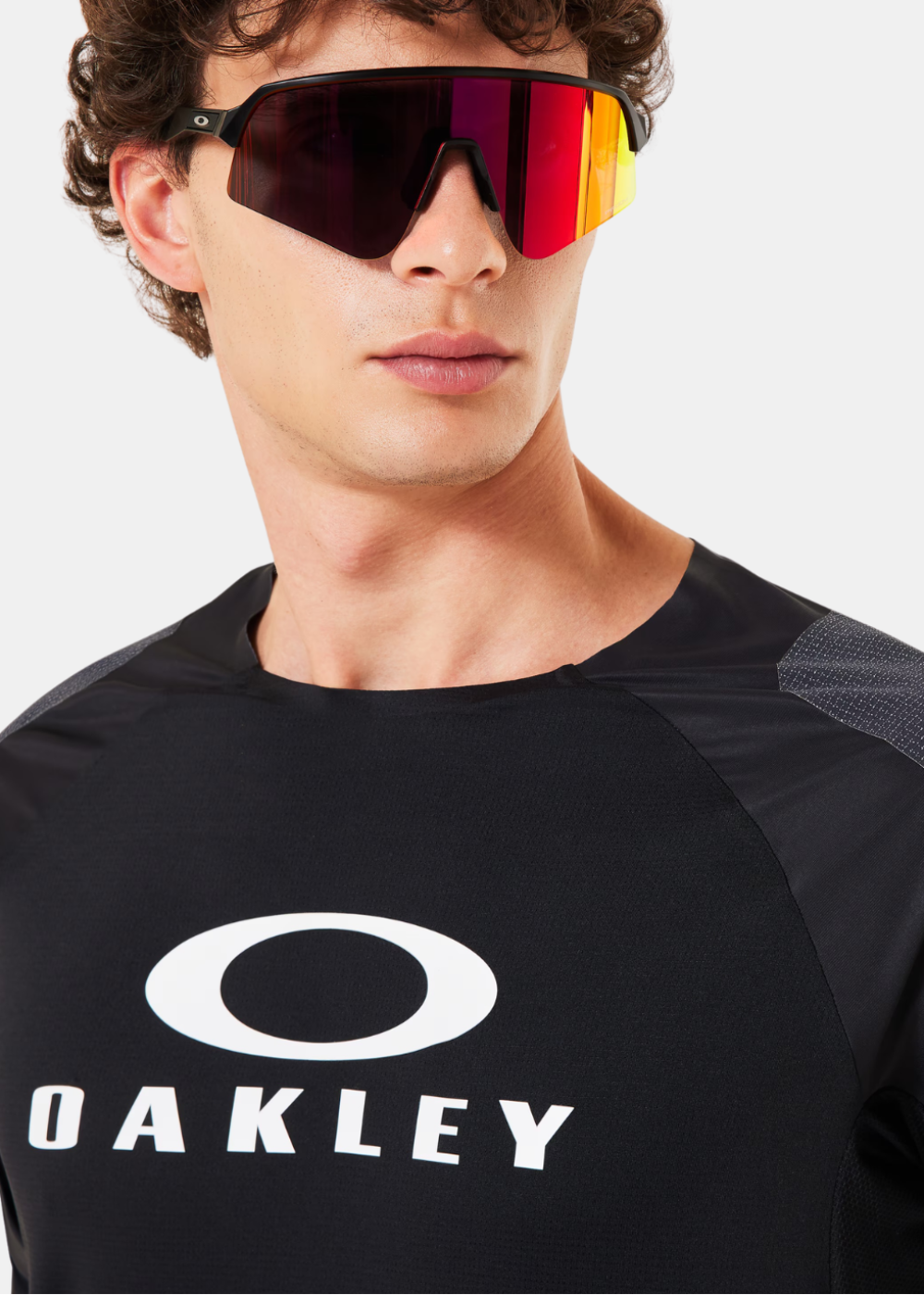 Gros plan sur le logo Oakley blanc et le col rond du t-shirt technique noir porté par un mannequin
