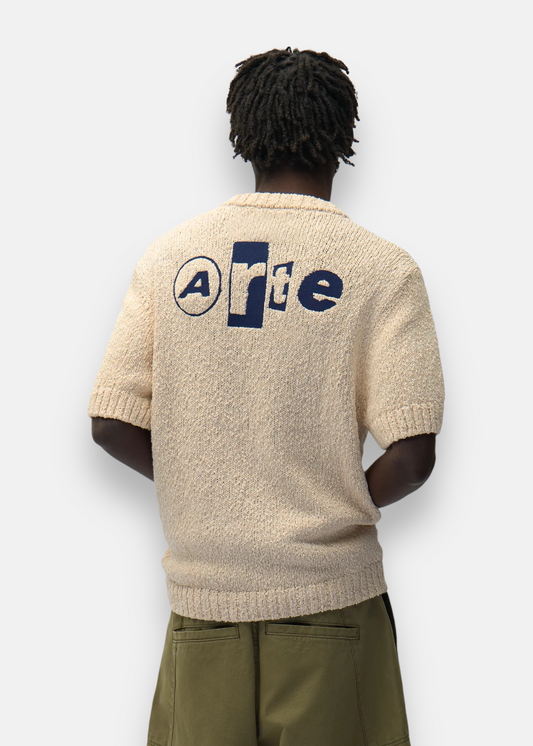 Homme de dos portant le t-shirt en maille beige Arte Antwerp, mettant en valeur le logo bleu et la texture knit.