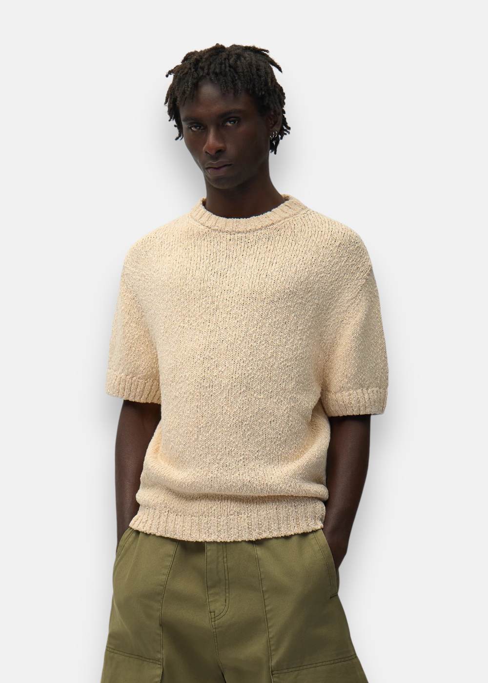 Vue de face d'un homme portant le t-shirt en maille beige Arte Antwerp à col rond avec les mains dans les poches.