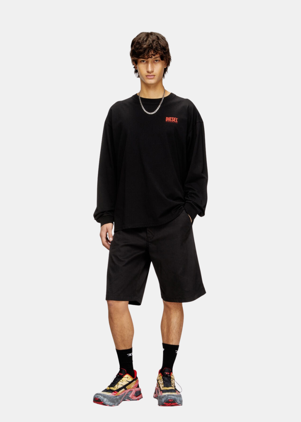 Look complet homme avec t-shirt manches longues noir Diesel, short noir, chaîne argentée, chaussettes hautes et baskets.
