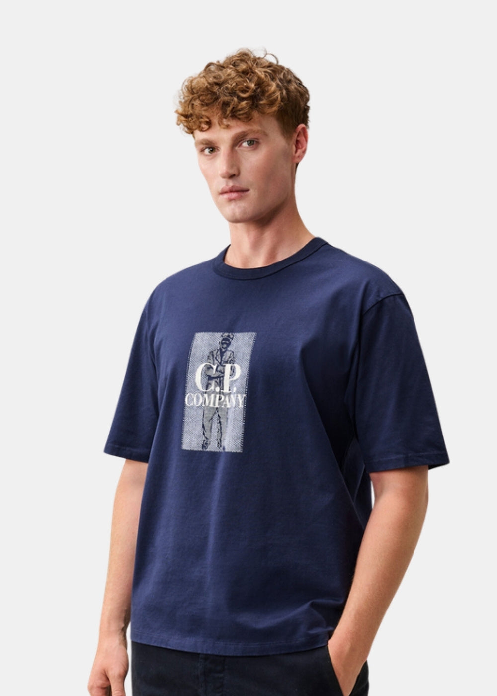 Porté de face d'un t-shirt marine C.P. Company à col rond, coupe classique, motif British Sailor au front, avec pantalon sombre.