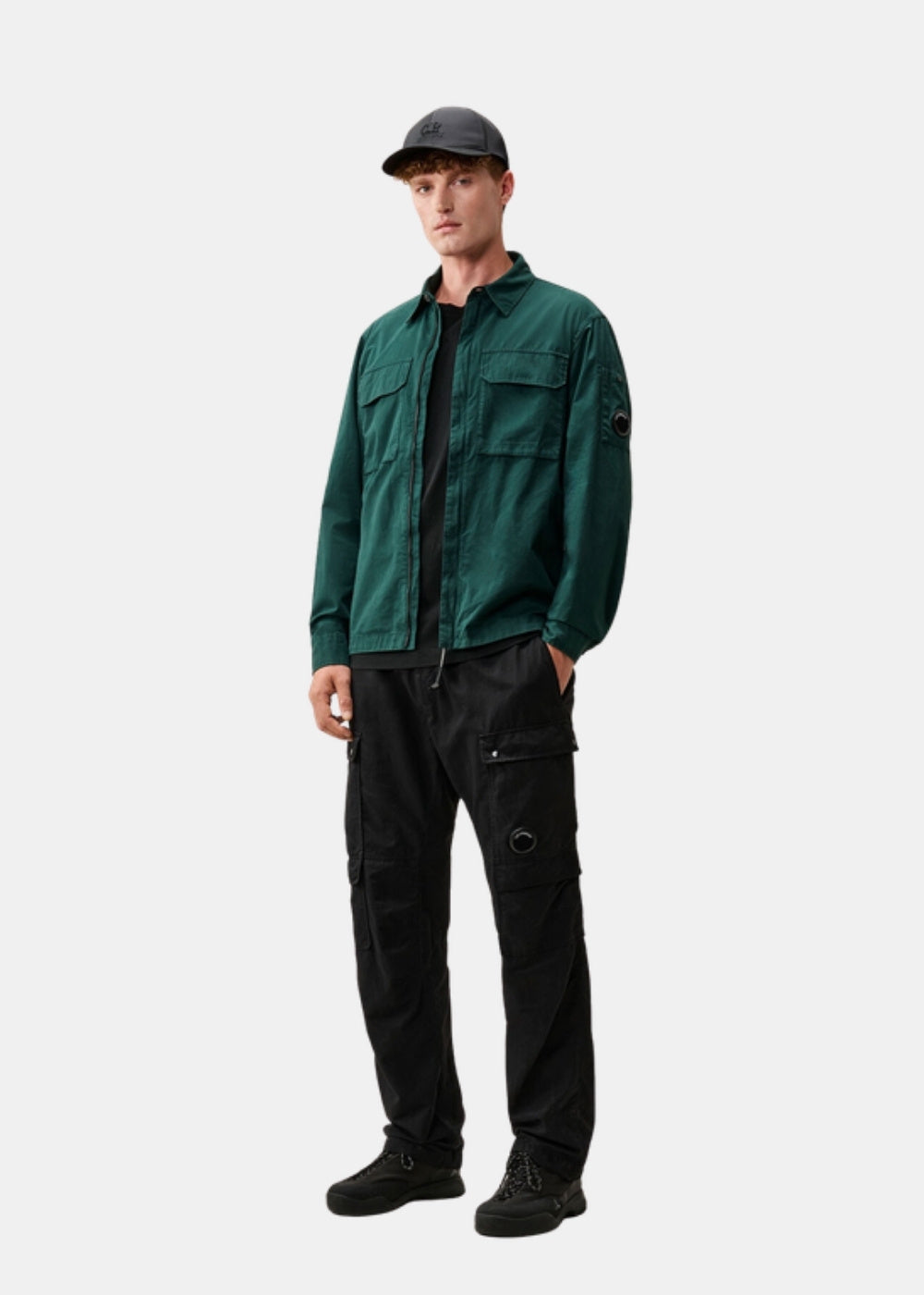 Porté en pied d'un look streetwear avec surchemise verte, pantalon cargo noir et casquette, illustrant un style de mi-saison.