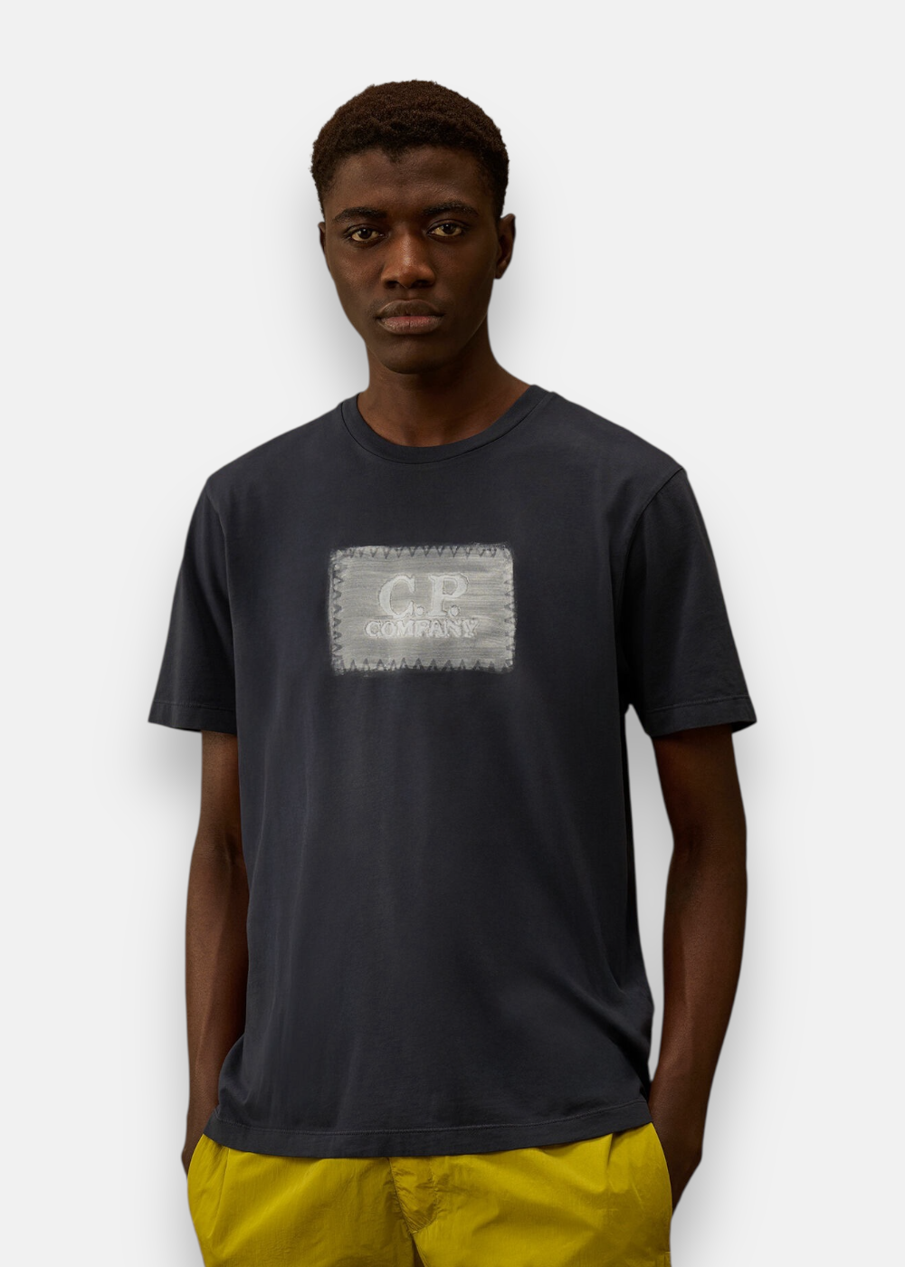 T-shirt bleu marine porté par un mannequin de face avec un pantalon jaune, logo brossé visible