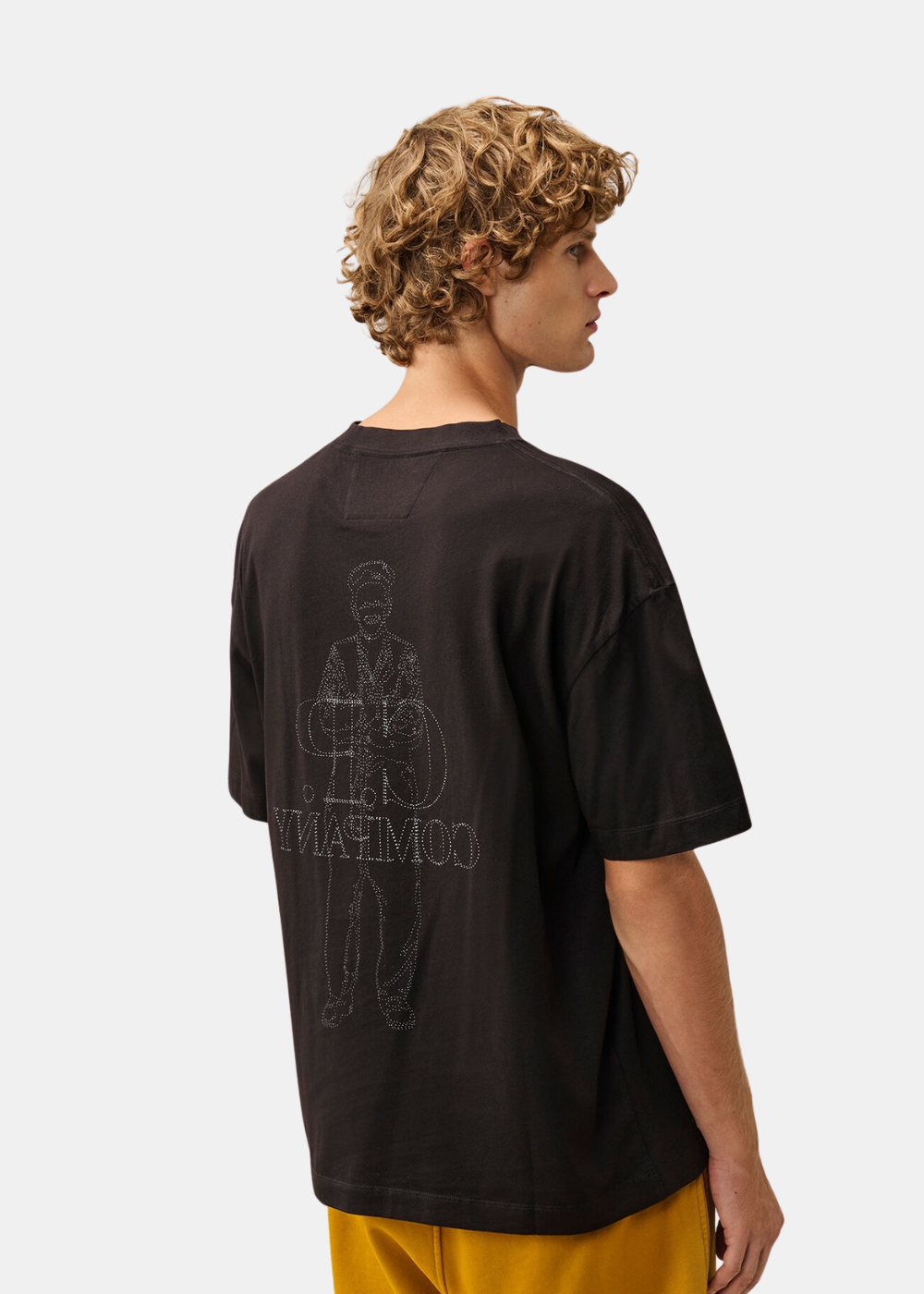Mannequin homme de face portant le t-shirt noir C.P. Company avec logo blanc sur la poitrine et pantalon jaune